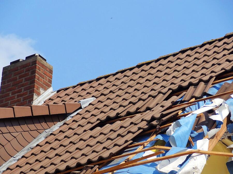 A tarp weighted over broken tiles on a roof after a storm